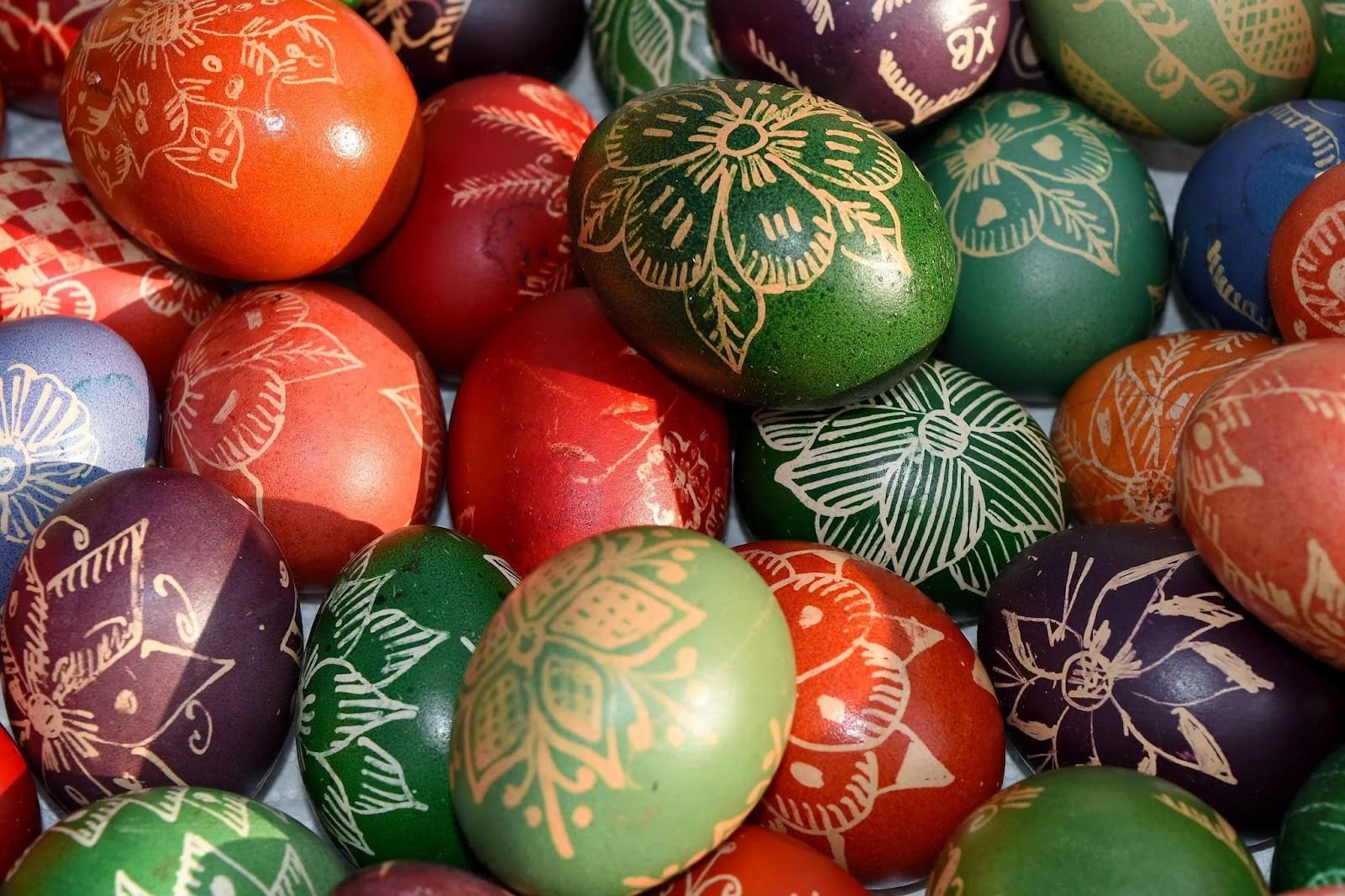 Close-up of colorful Easter eggs dyed in red, green, orange, and purple with intricate floral and decorative patterns.
